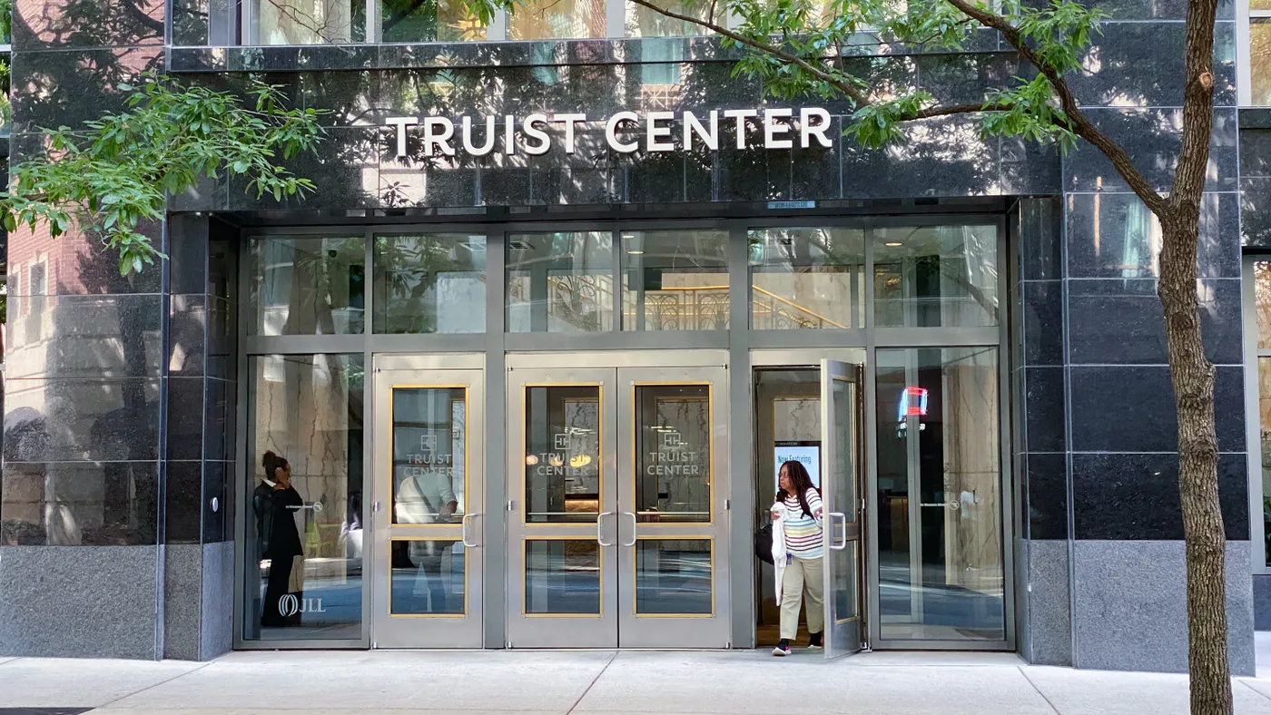 A person walks out through the glass doors of an office building with the words "Truist Center" above the entrance.