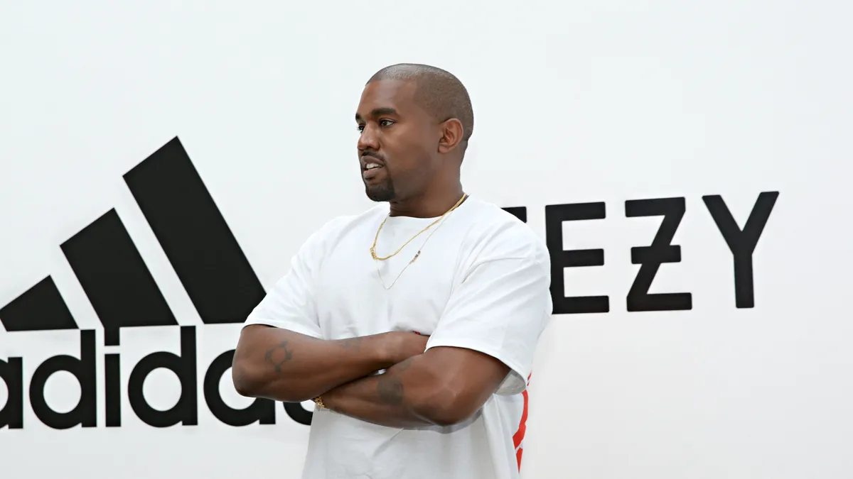 Kanye West stands in front of Adidas and Yeezy logo.