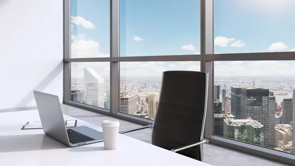 A workplace with laptop and a cap of coffee in a modern panoramic office