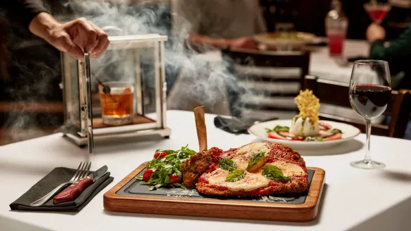 An image of a veal parmesan chop with marinara sauce and mozzarella on a dark table.