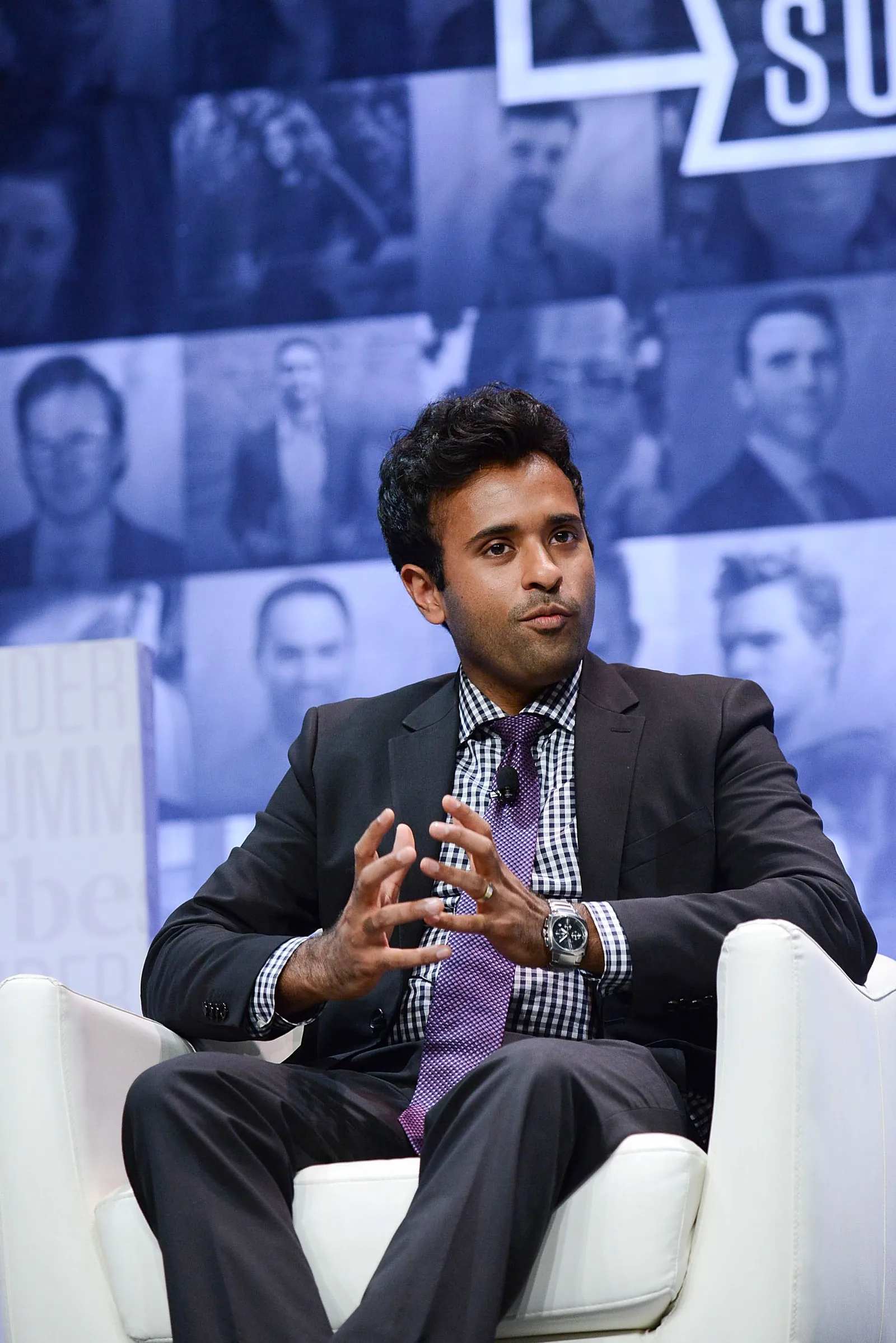 Vivek Ramaswamy sits in a chair on a stage gesturing with his hands