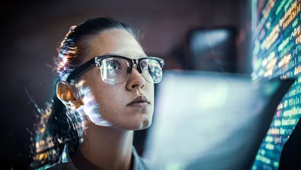 A worker wearing glasses looking at code on a wall.