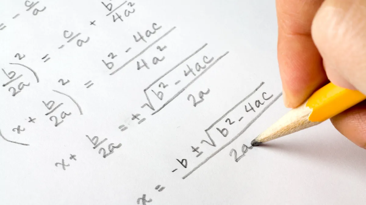 A hand holding a pencil is shown writing out algebra equations.