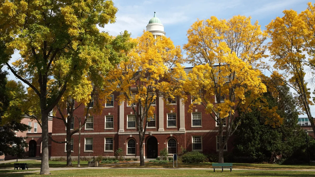 A large brick academic building surrounded by trees with red, orange and yellow leaves.