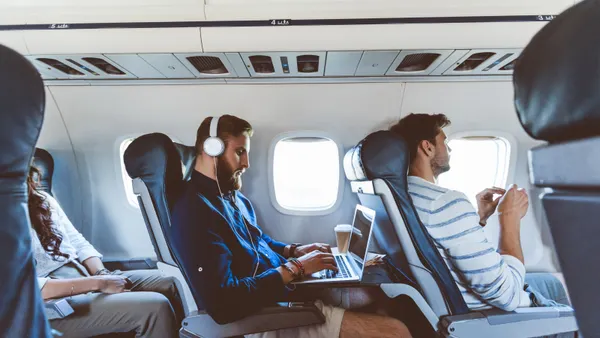 Young bearded man sitting inside an airplane and using a laptop.