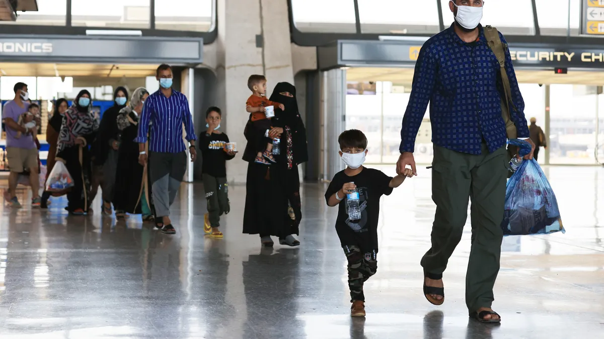 People of all ages arrive at an airport wearing masks and carrying bags and water bottles.