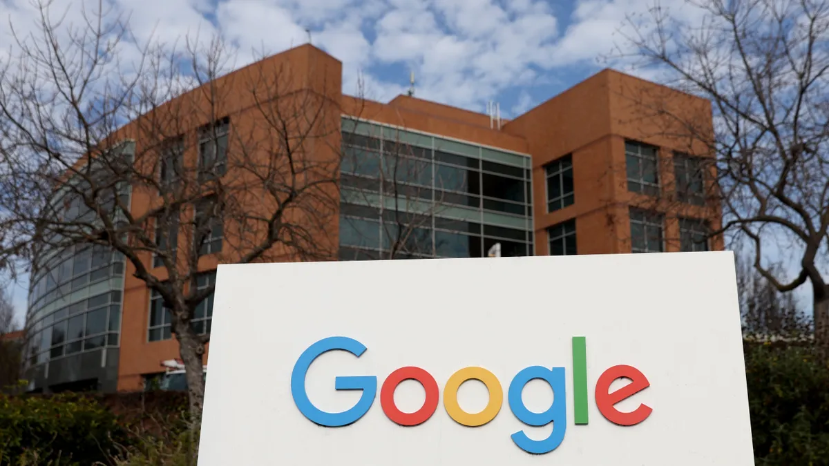 Google sign in front of a building with a blue sky and clouds in the background.