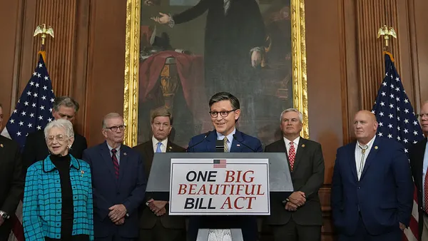 Speaker Mike Johnson stands behind a podium in front of a portrait of George Washington.