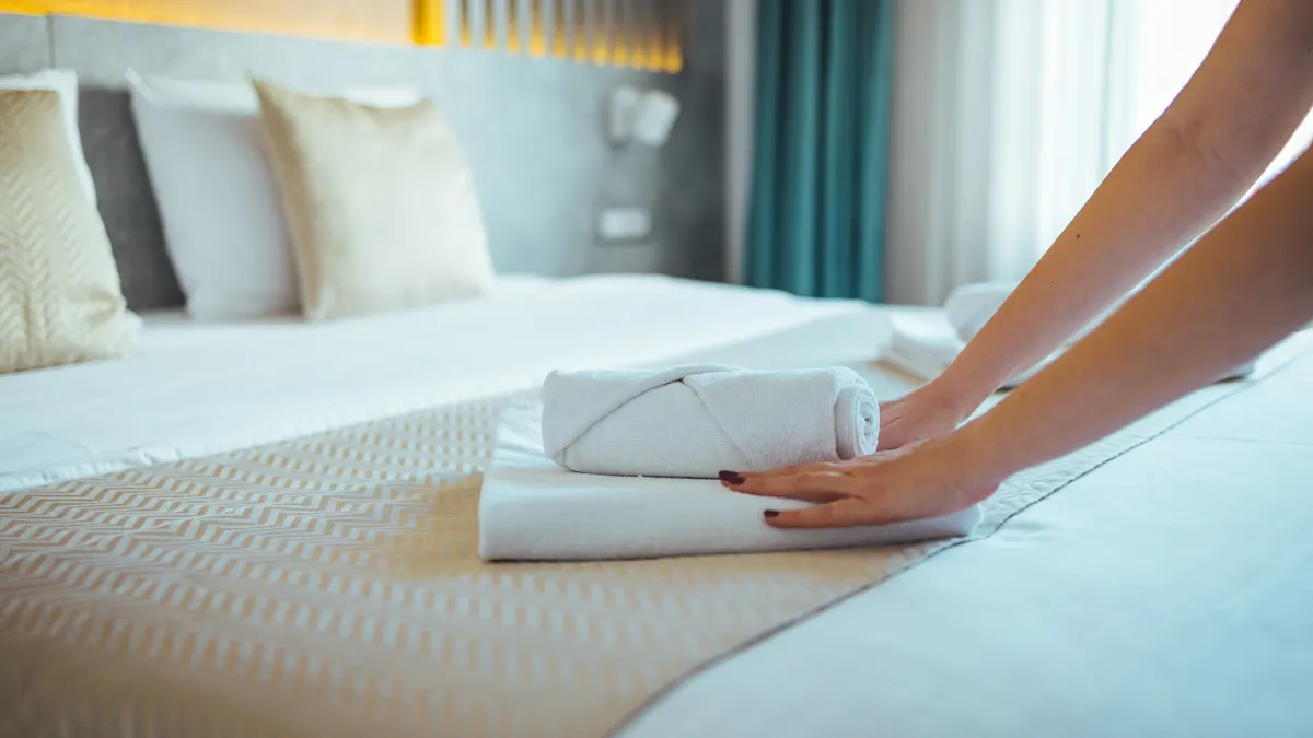 Hands place fresh towels on a hotel bed.