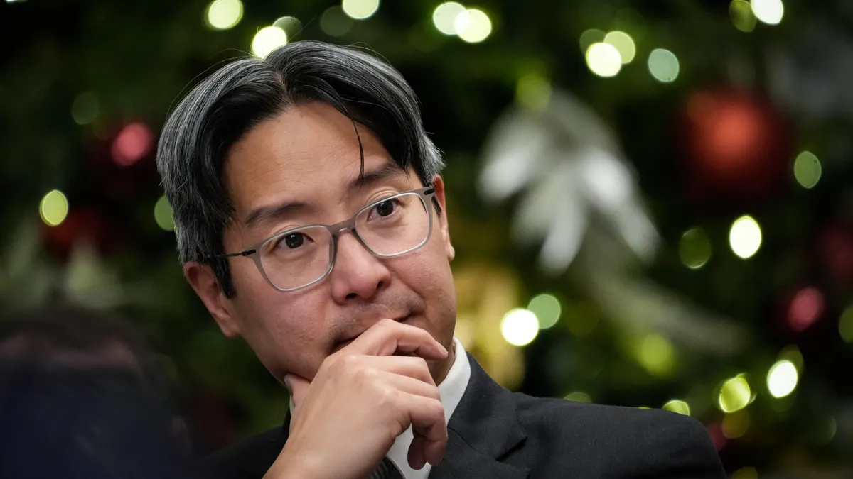 michael hsu acting head of the OCC rests his chin on his hand in front of a christmas tree at a federal regulatory meeting