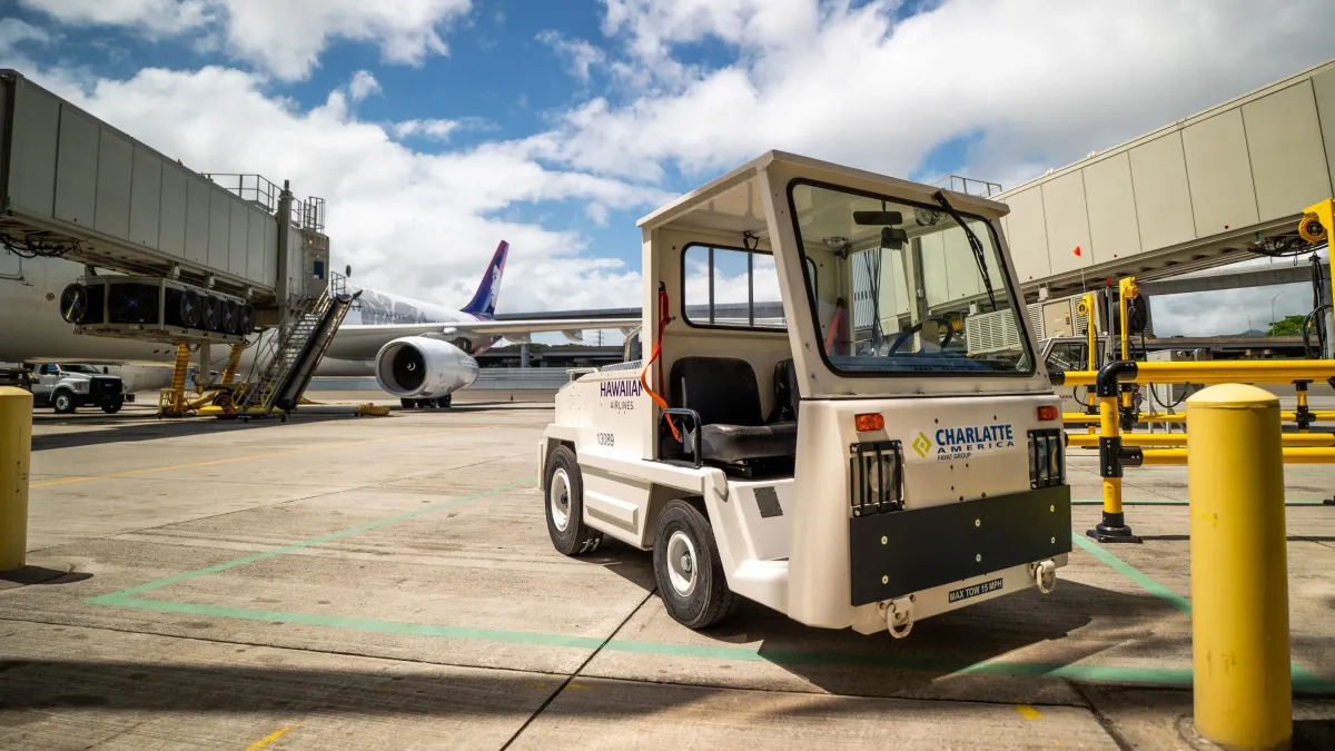 A Hawaiian Airlines ground support vehicle sits on the tarmac near a Hawaiian Airlines aircraft
