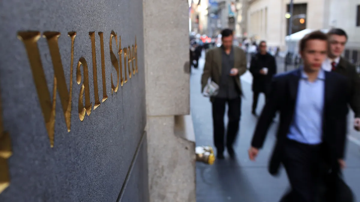 Image of business people walking past building with Wall Street sign.