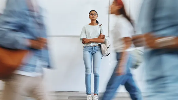 A woman stands against a wall while blurred people walk past her in the foreground.