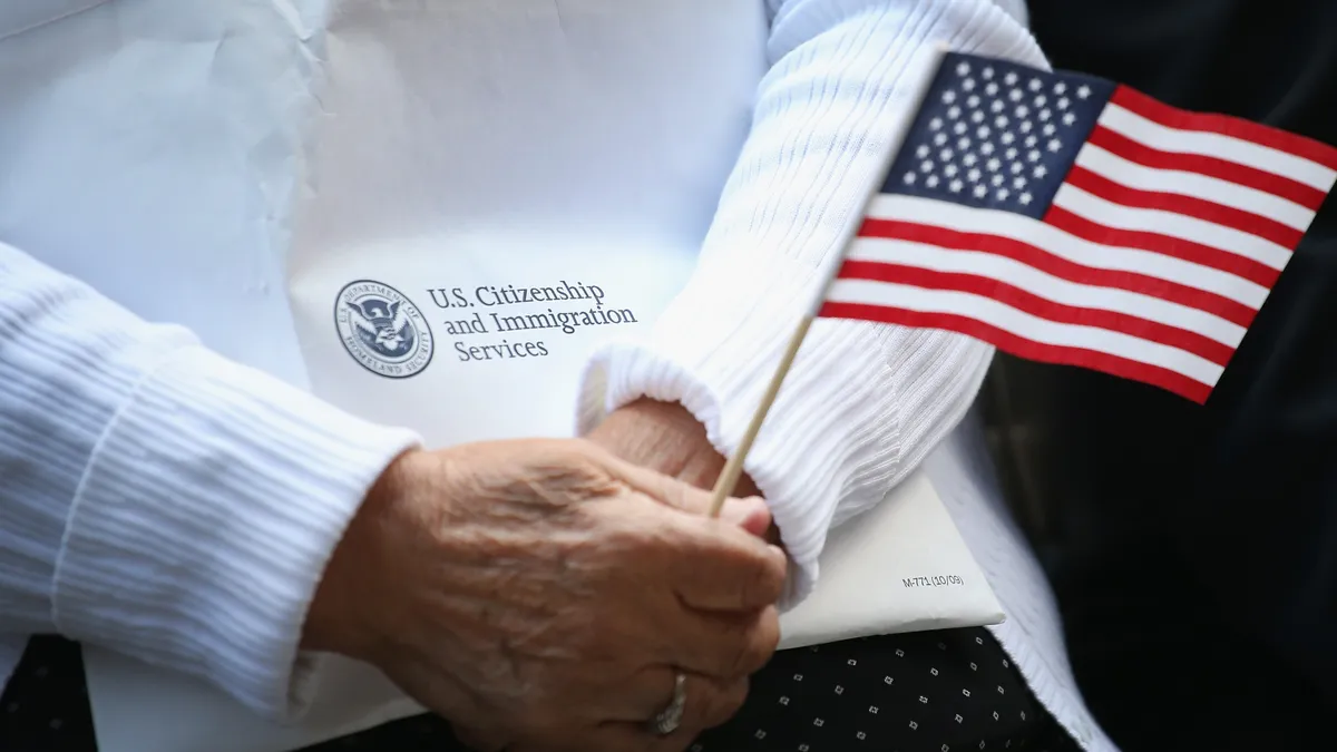 A pair of hands holding an American flag and a piece of paper saying, "U.S. Citizenship and Immigration Services"