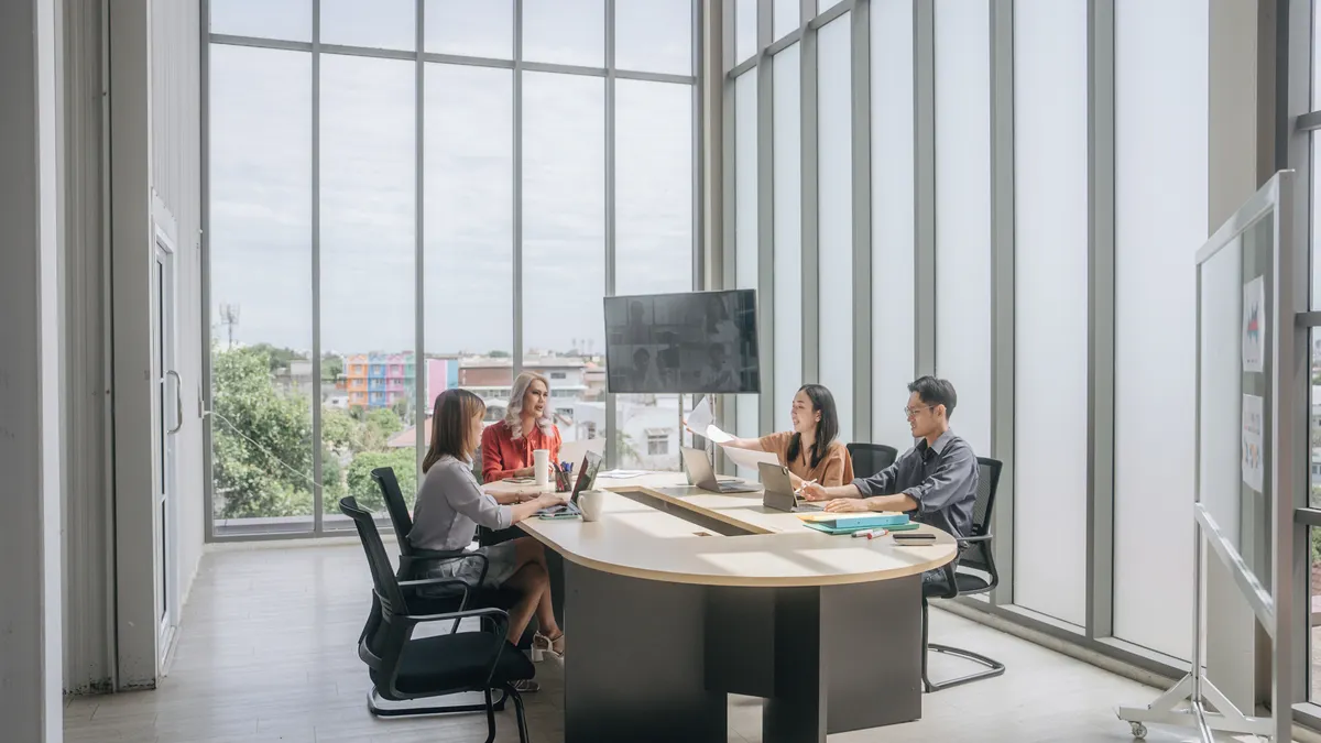 Group of business people having a meeting in a conference room with tall windows.