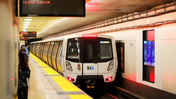 A white-painted subway train arrives at an underground station with several people standing on the platform.
