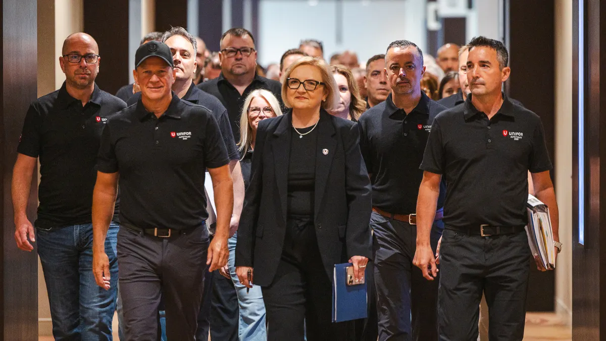 Over a dozen Unifor union members walk down a hall, wearing matching black shirts, with leaders at the front.