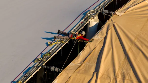 A construction worker lies across a gap and pulls a large piece of fabric.