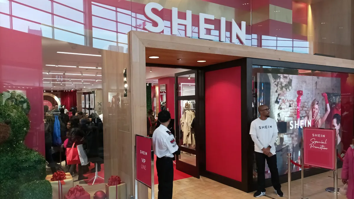 A Shein popup storefront. Two people stand in front of the doors wearing Shein T-shirts.