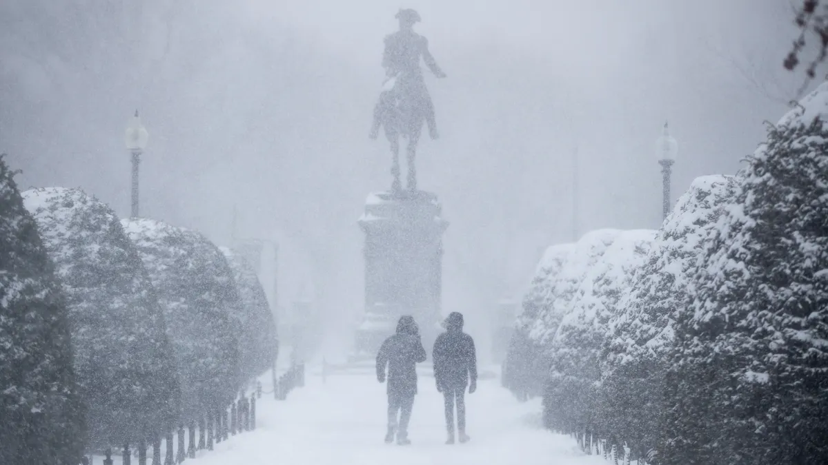 Shadowy figures walk toward a statue of a person on a horse in a snowstorm.