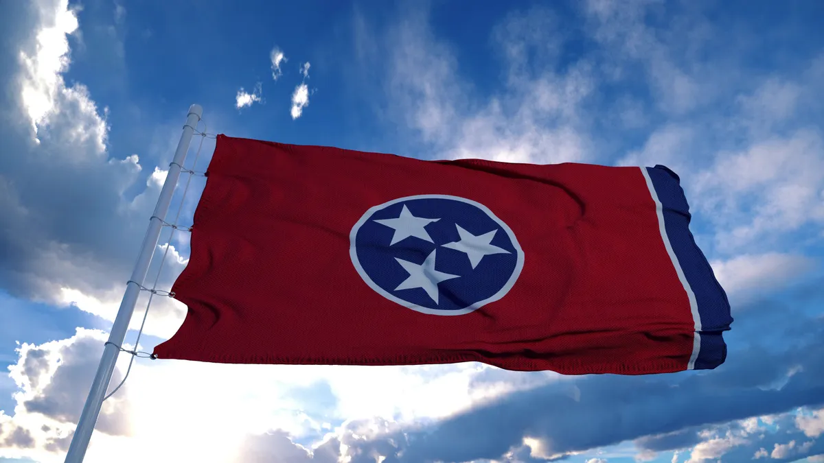 Tennessee state flag on a flagpole waving in the wind with a blue sky background.