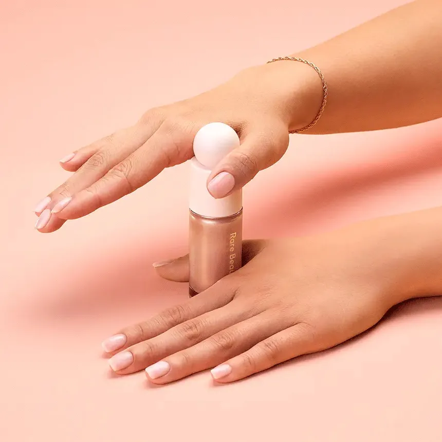 A person using two hands to open Rare Beauty&#x27;s Positive Light liquid luminizer.