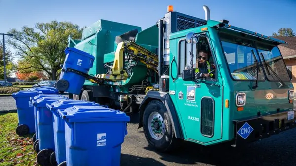 A side-loading trash truck grabs a recycling cart