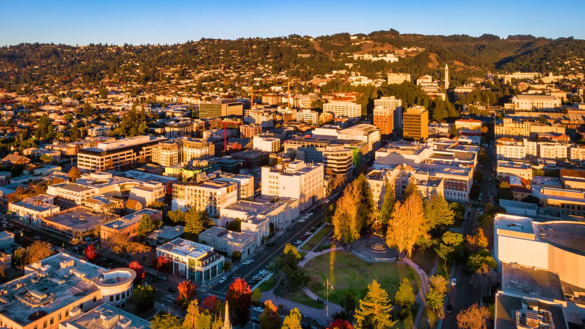 Aerial shot of buildings in a downtown. A tree-covered hill sits in the background.