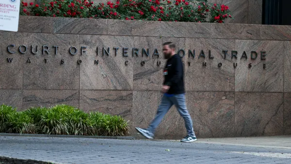 A person walks on a sidewalk near a wall that has letters spelling out "Court of International Trade Watson Courthouse."