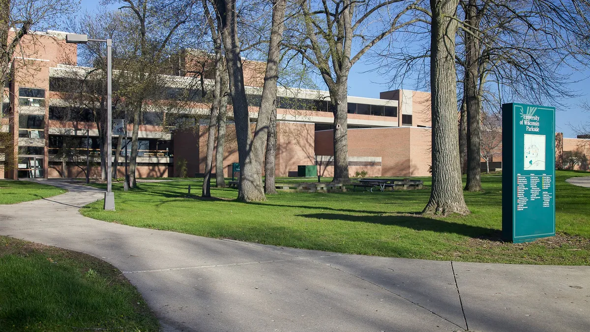 A wide shot of UW Parkside, featuring a building in the background with a gray path leading to it with nearby trees.