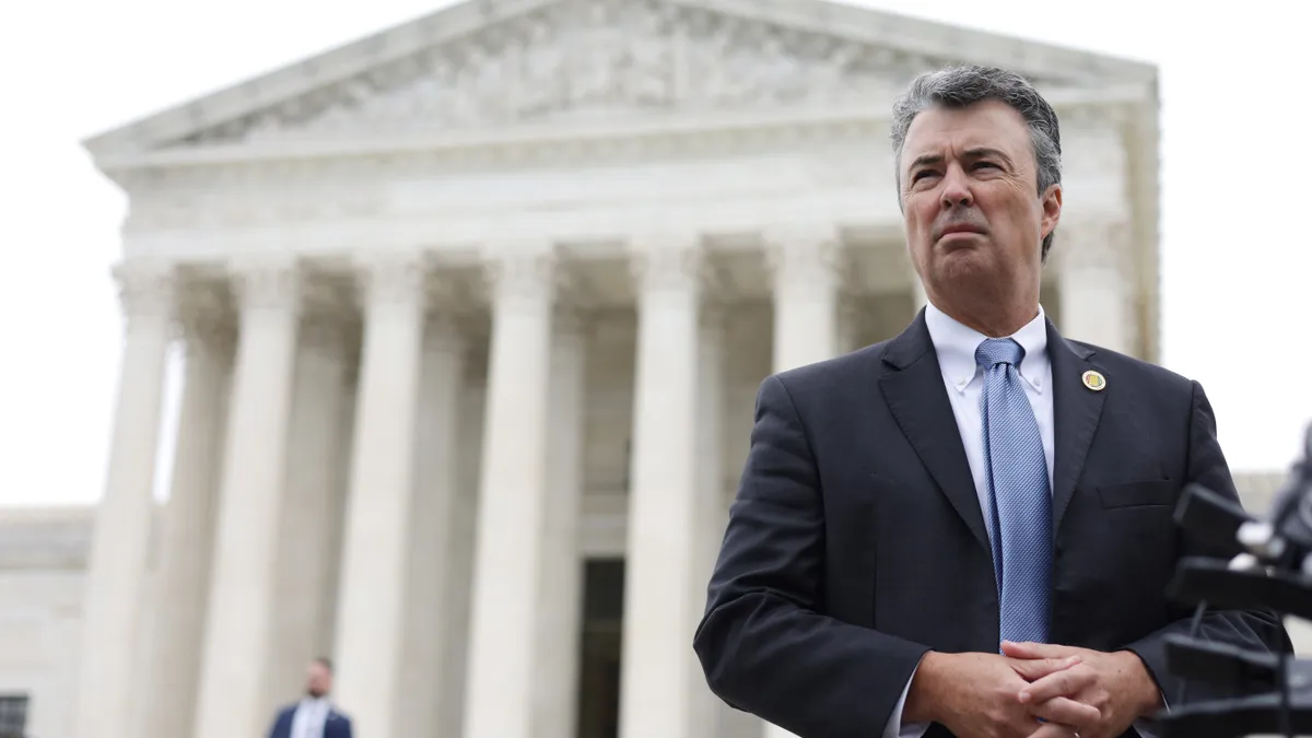 In a suit, Steve Marshall stands to the right side of the photo with folded hands, with the U.S. Supreme Court in the background.