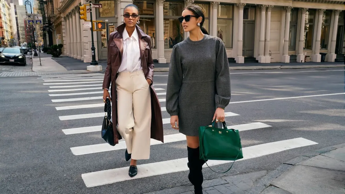 Two fashionable looking people, wearing sunglasses, cross a street in a crosswalk.