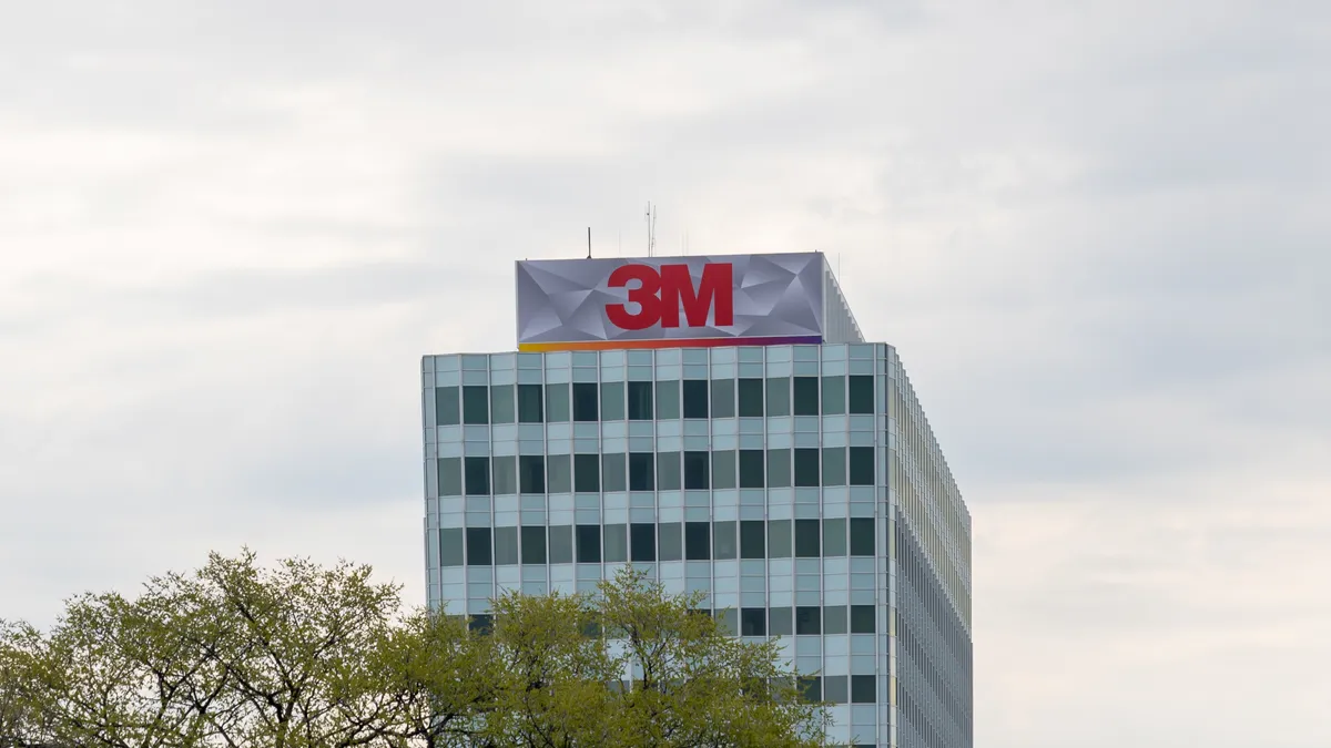 A light-blue and whit building with dark windows and the red 3M sign on top of it on a cloudy day.