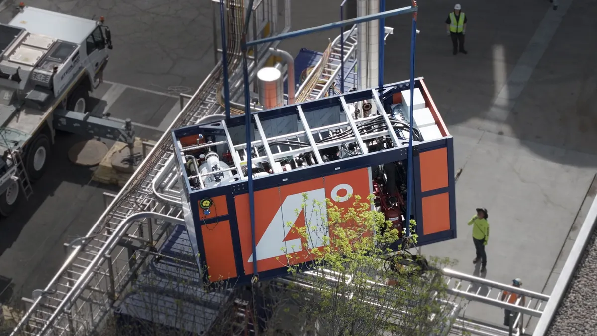 A piece of industrial equipment is lowered into place, with workers on the side