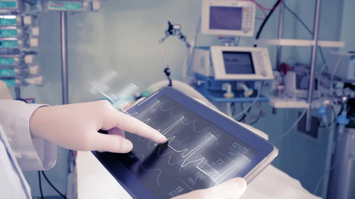 Gloved hand touching a medical device that shows heart rate in a medical facility.