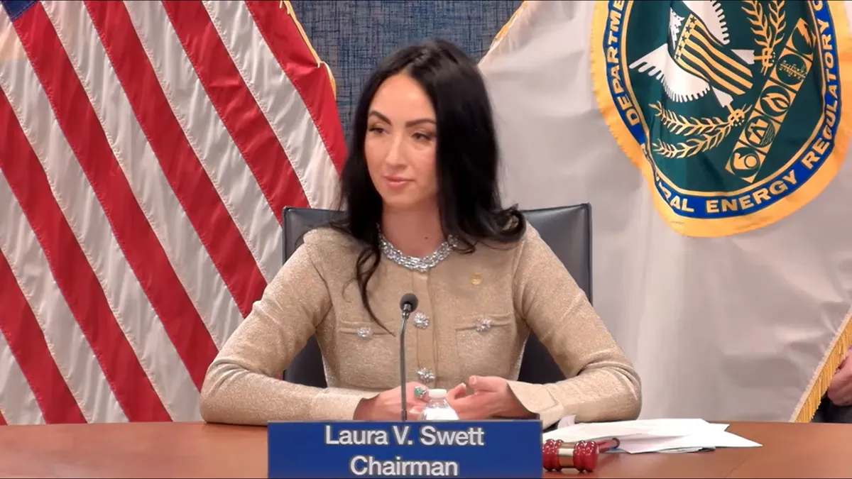 A woman sits at a desk in front of two flags.