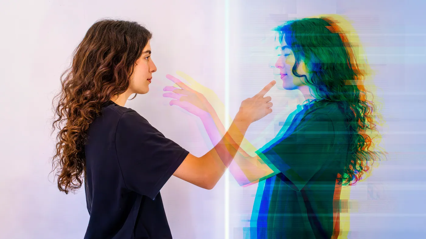 A young woman faces her digital twin, reaching out to make contact.