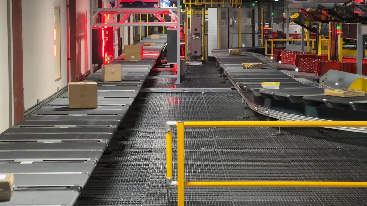 Packages move on a conveyer belt in a warehouse, with other machinery operating in the background.