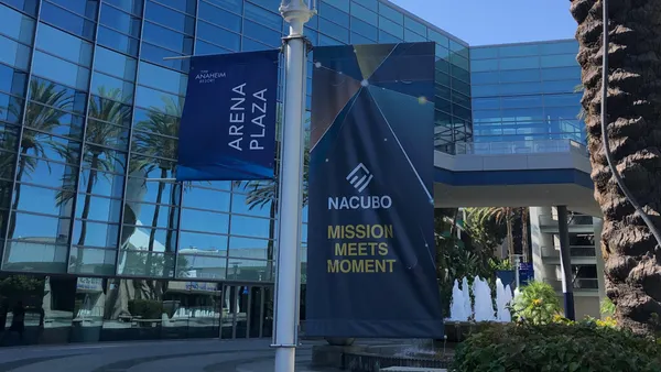 A sign in front of conference center with glass exterior, with palm trees in foreground.