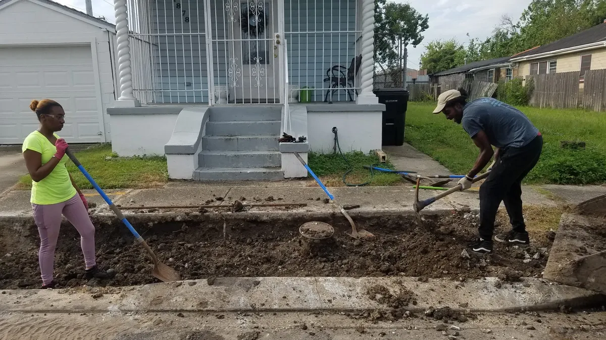 Man and woman digging a trench in front of a home.