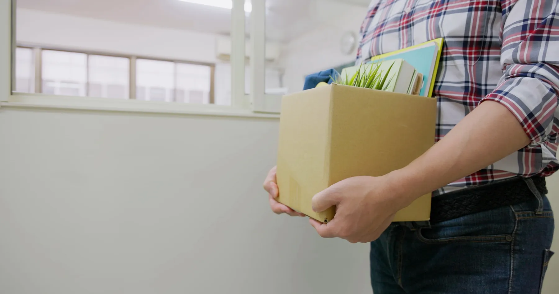 An adult holds a box full of office supplies on their way out of a classroom.