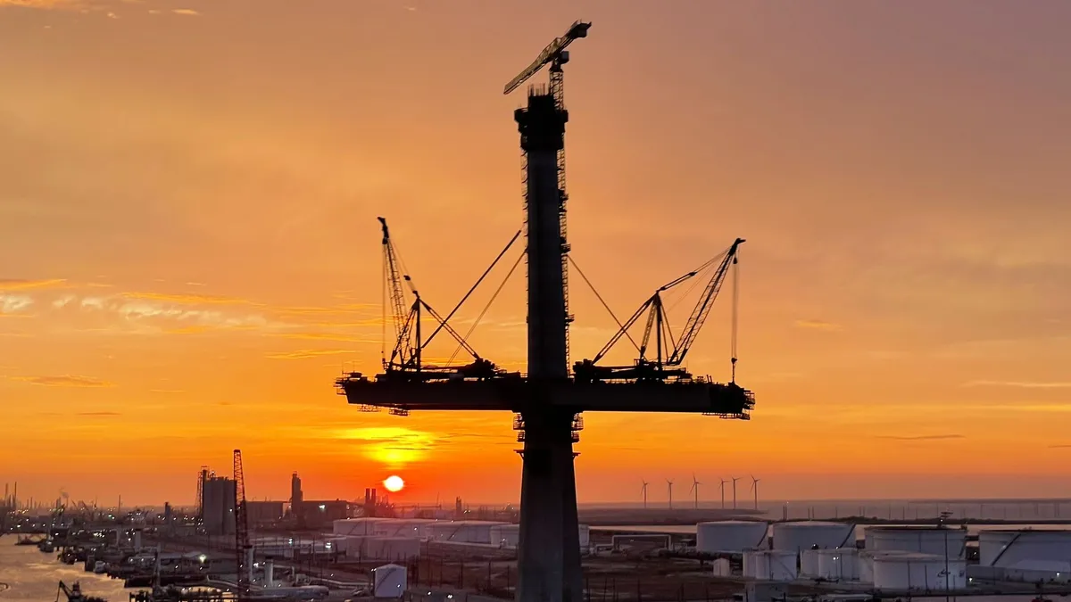 A bridge pylon and crane in Corpus Christi stand silhouetted against an orange and yellow sky.