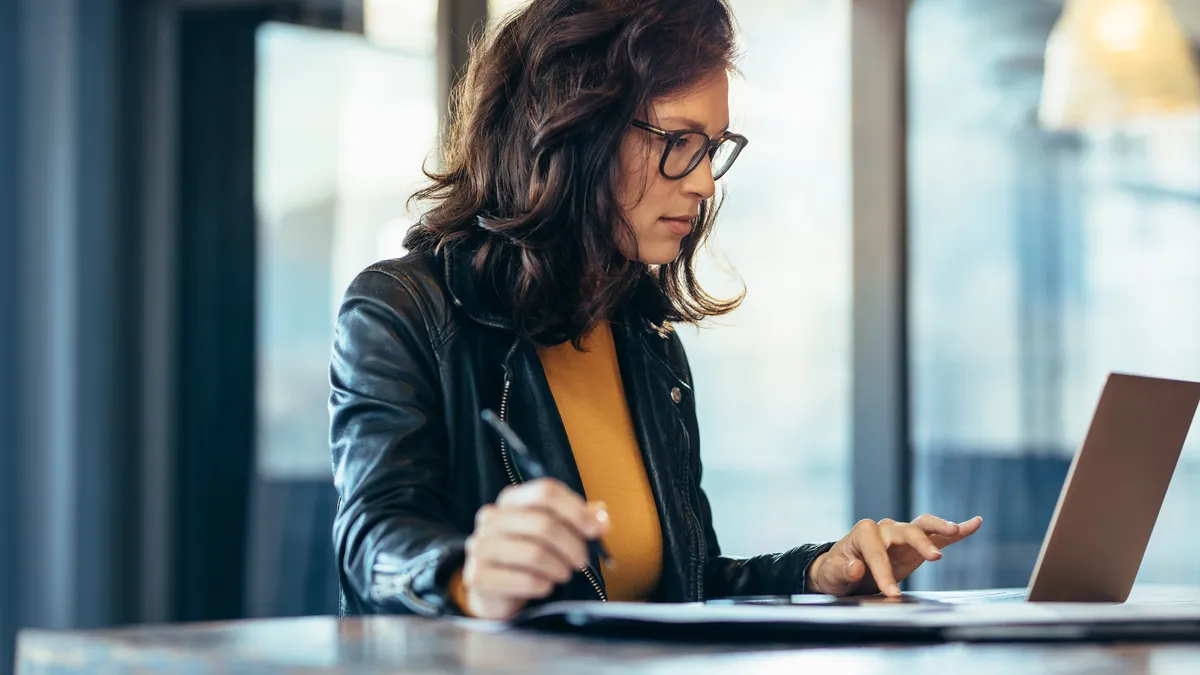 Businesswoman making notes looking at a laptop