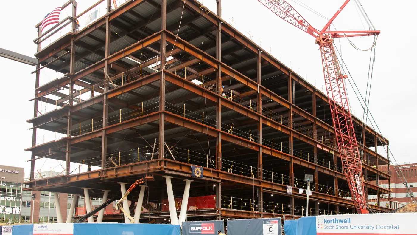 A steel skeleton of a tall building in the gray day rises in the foreground. It sits on an active construction site.