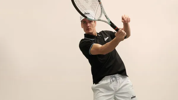 A man waves a tennis racket and wears tennis clothing.