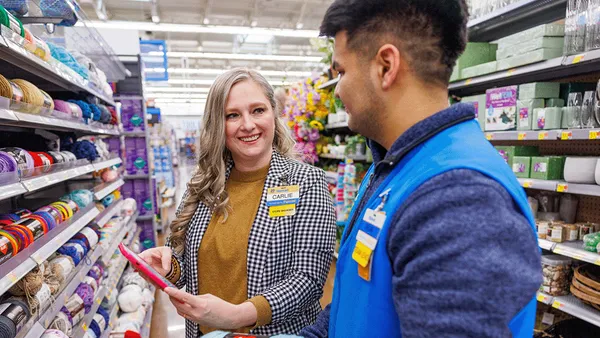 Two Walmart employees inside a store look at a handheld tablet