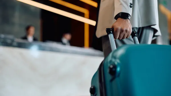 A hotel guest rolls a suitcase toward a front desk.
