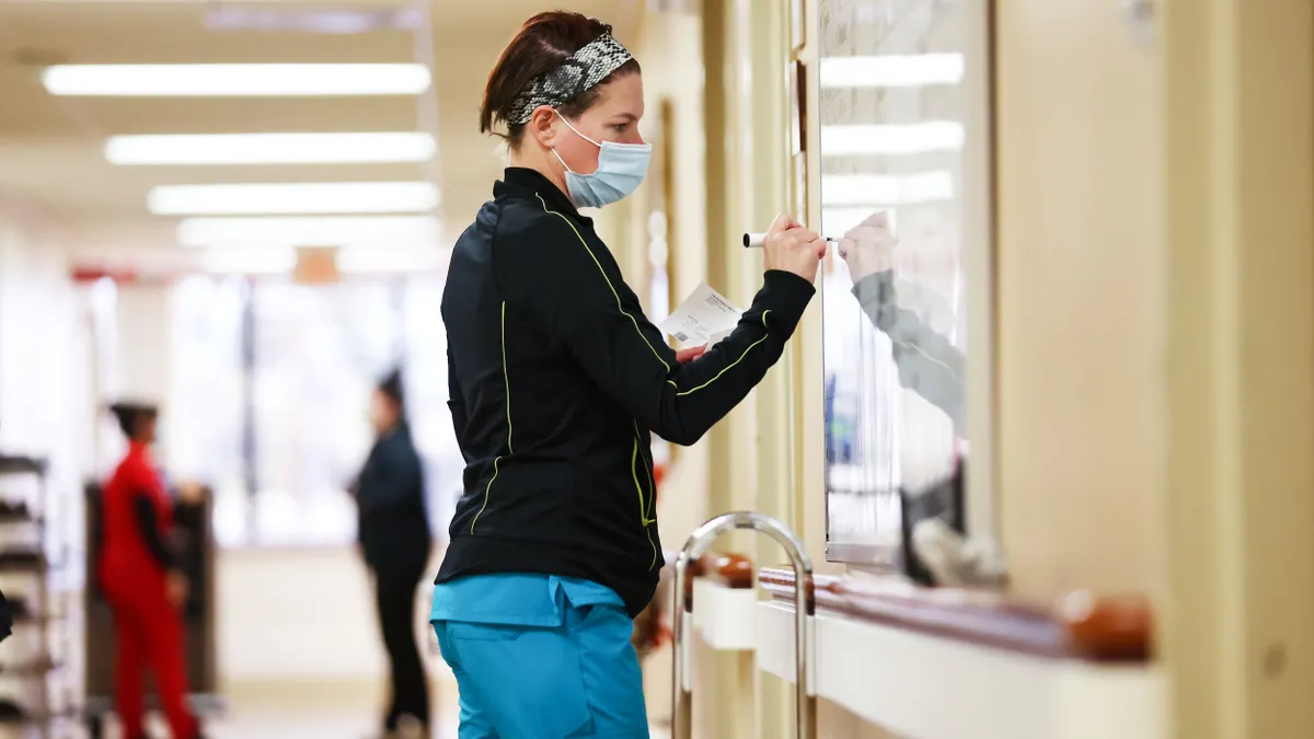 A person wearing scrubs writes on a white board.