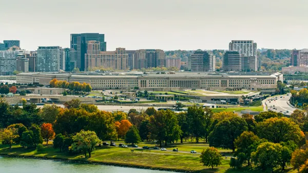 A view of several office buildings from a distance across a river and over many trees.