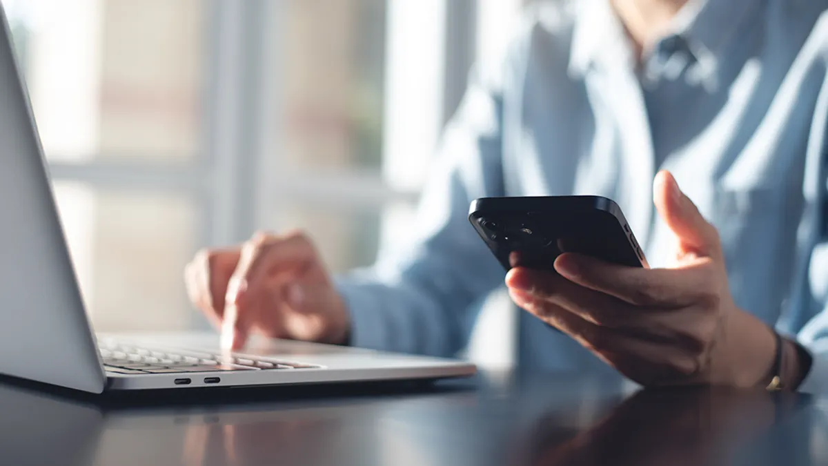 A hand with a phone in it and laptop in frame.